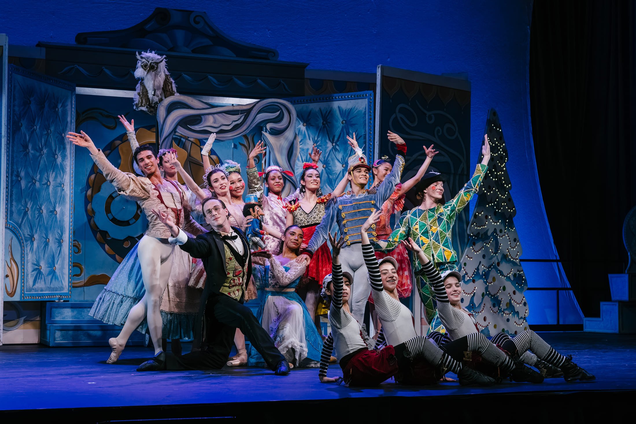 Group of performers in theatrical costumes on a brightly lit stage.