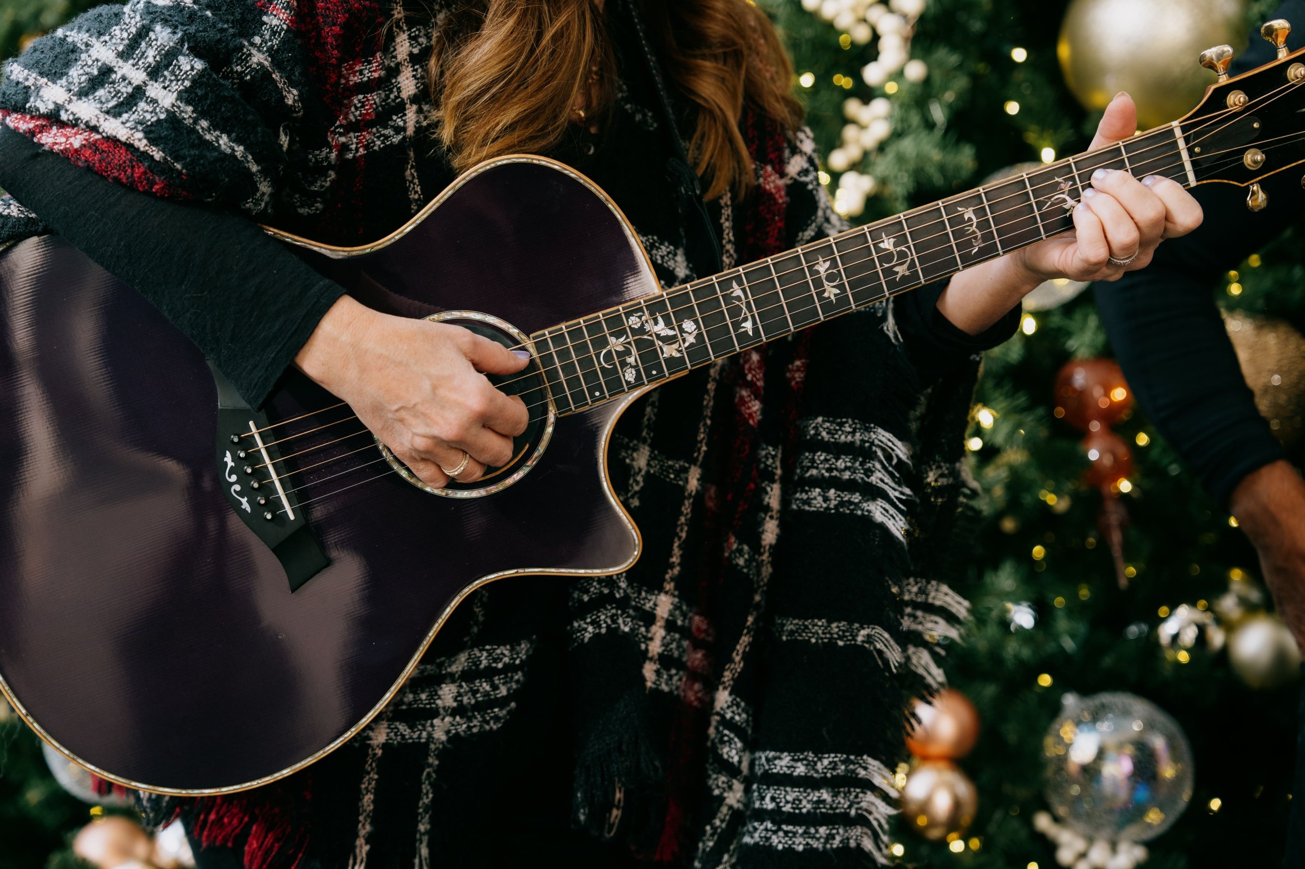 Close-up of a person wearing a plaid jacket playing an acoustic guitar.
