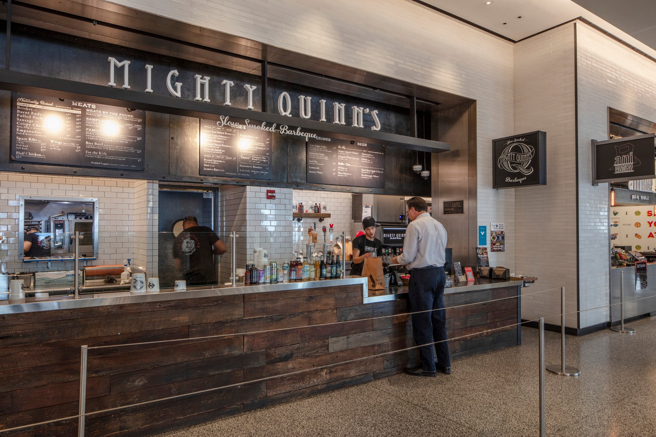 Man ordering food at a brightly lit, modern café or food counter with a wooden accent wall.