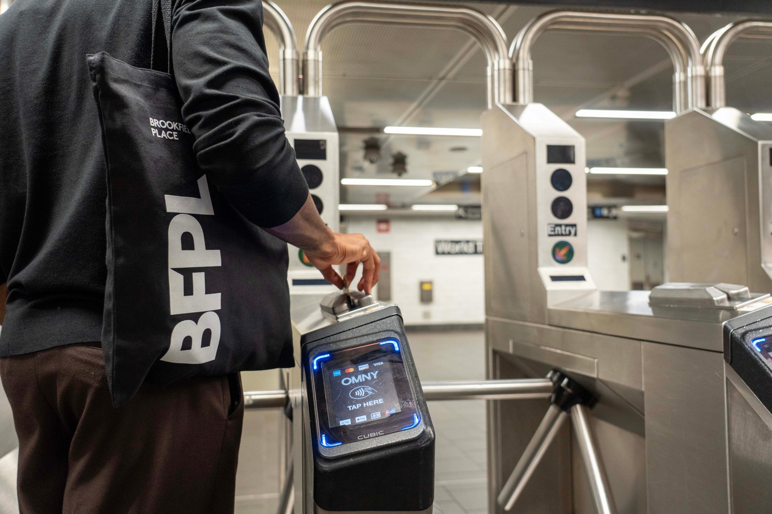 Person scanning a black phone or card at an subway turnstile entry point.