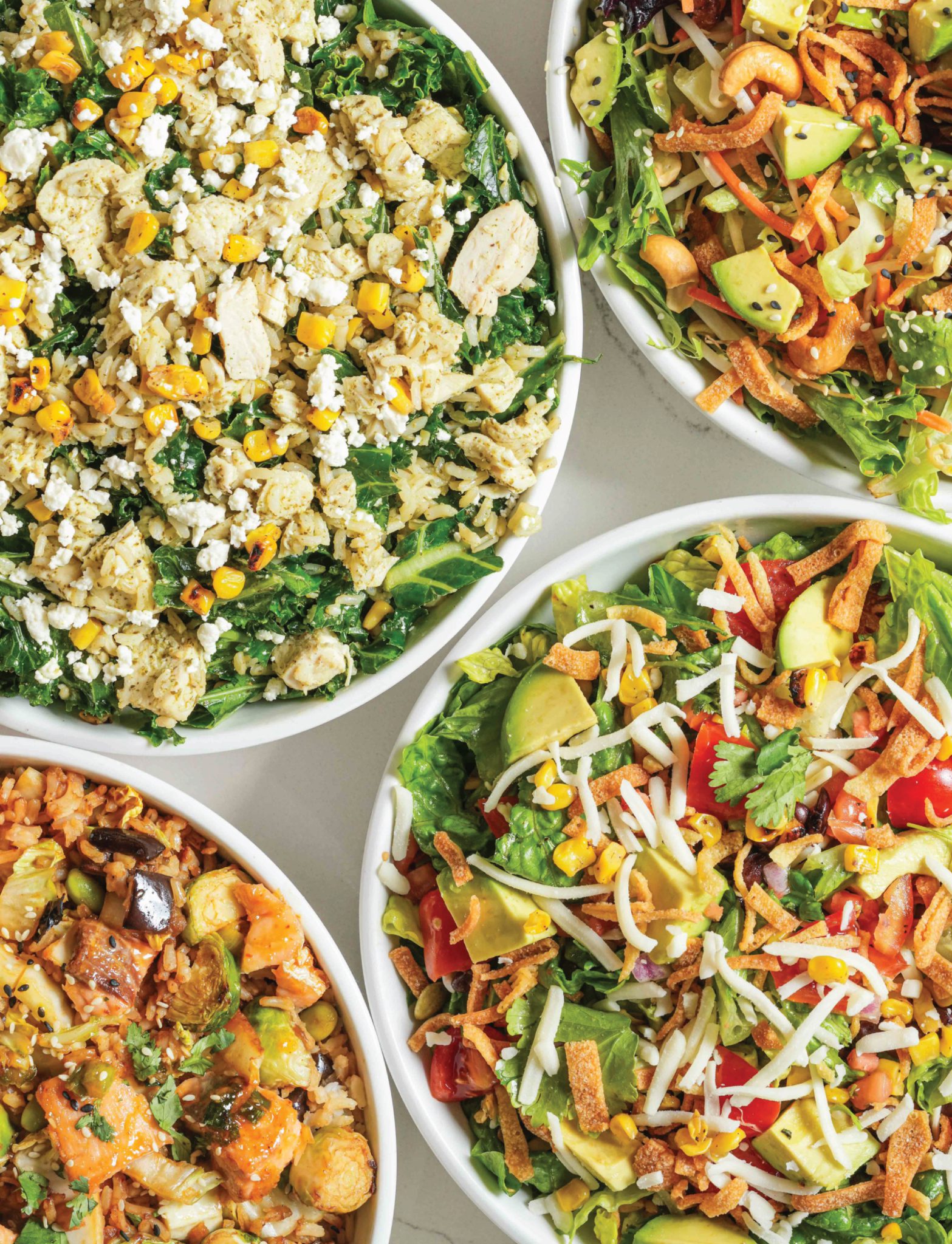 A close-up, top-down view of four bowls of healthy food from Carrot Express, featuring various salads and grain bowls rich in vegetables, proteins, and colorful toppings.