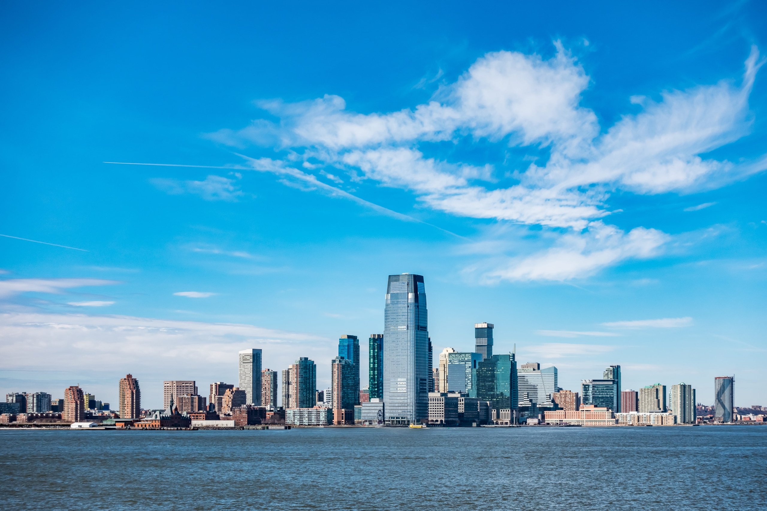Panoramic view of the New York City skyline across the Hudson River on a clear, blue-sky day.