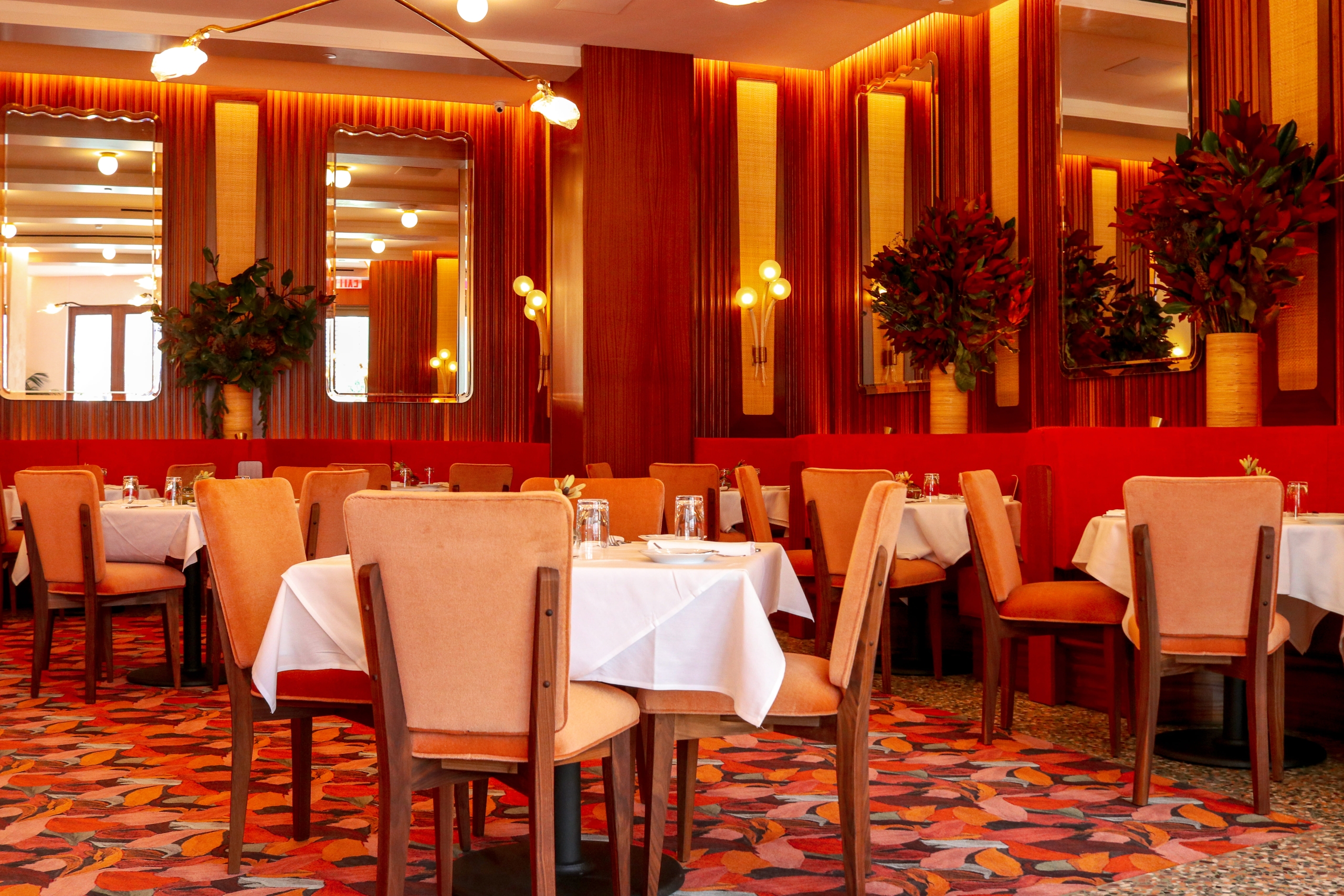 Restaurant interior featuring red velvet upholstery, dark wood paneling, and warm, golden lighting.