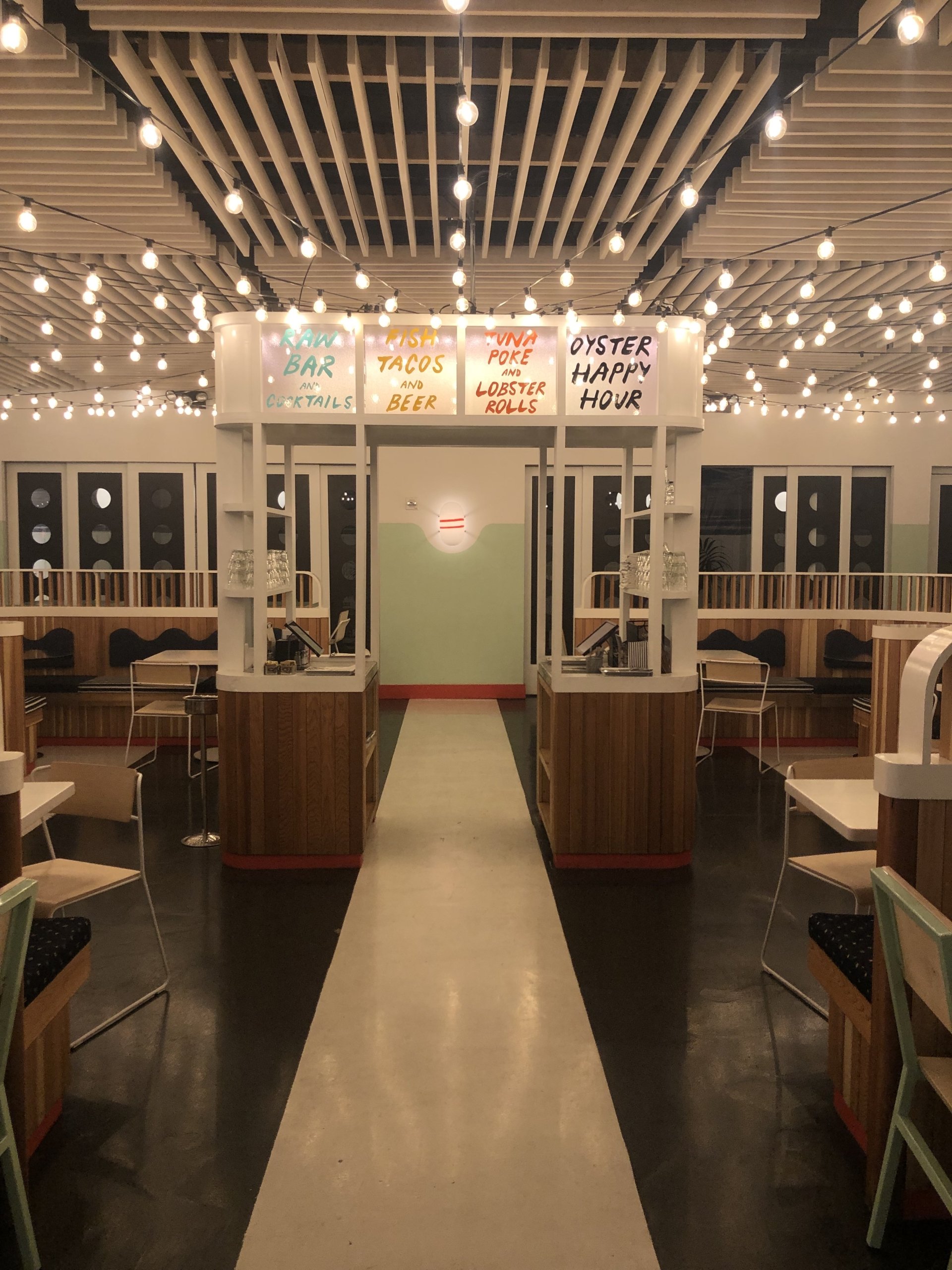Elegant, dark-toned restaurant interior with white tablecloths, modern lighting, and wall paneling.