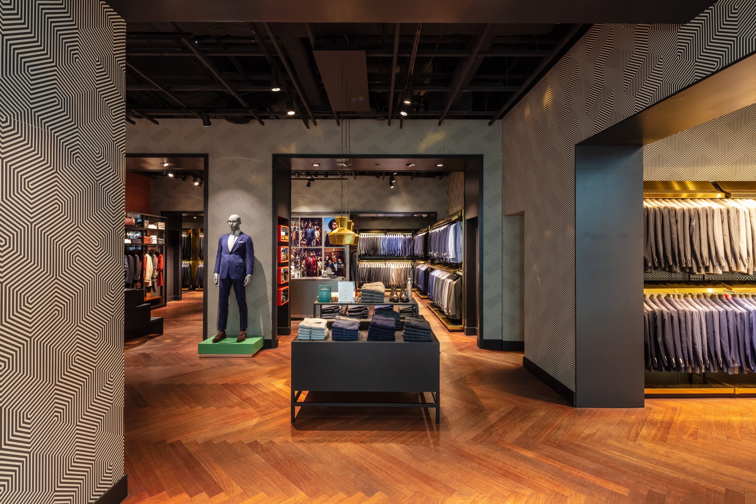 Retail store interior with mannequins, clothing displays, and a view into another section.
