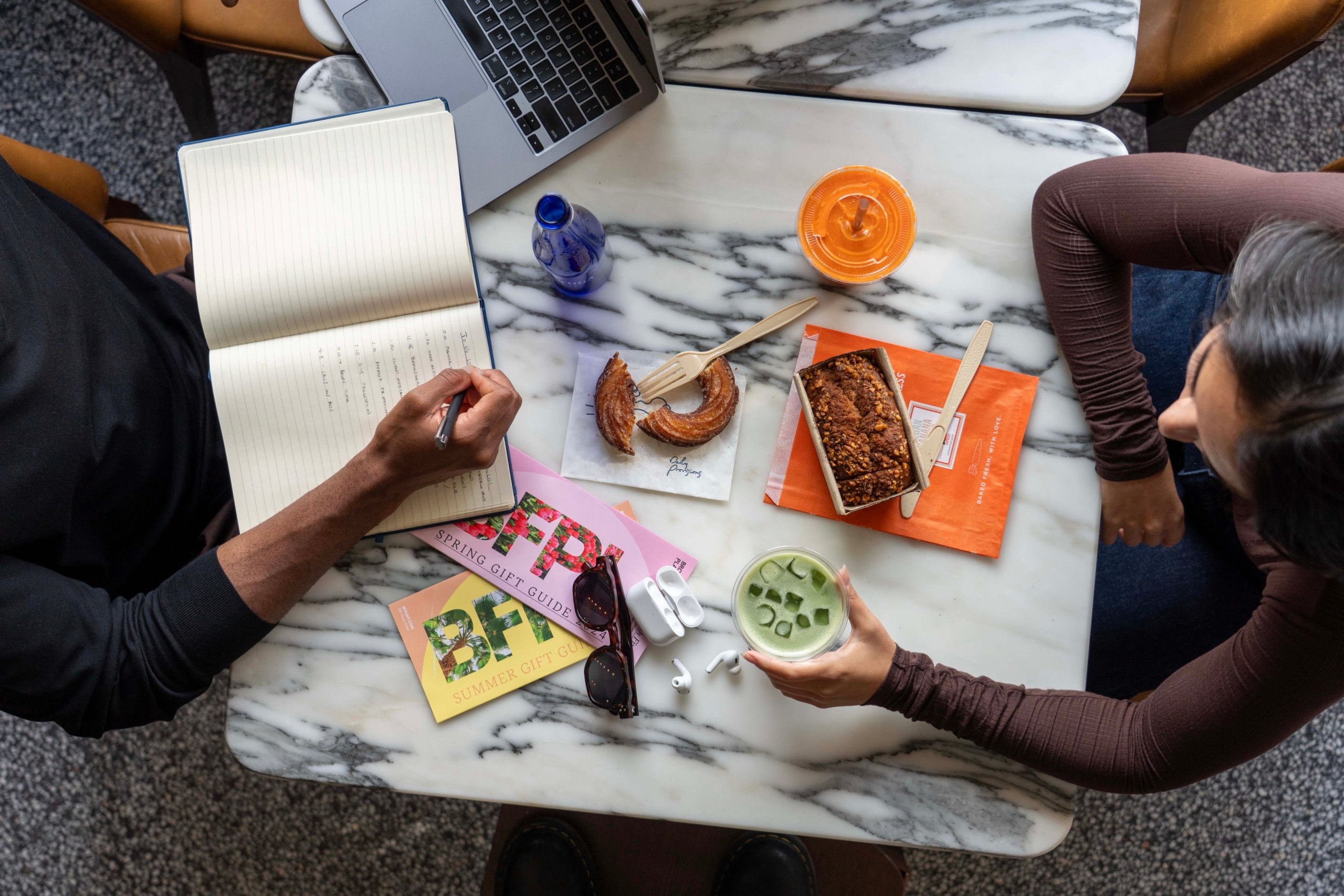 Two people seated at a table writing in journal and having a snack