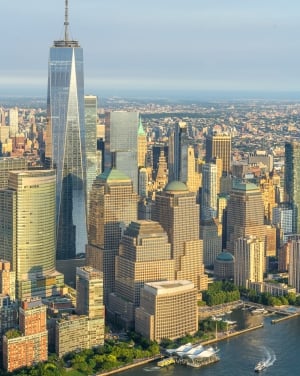 A vertical, aerial photo of the New York City skyline, focusing on One World Trade Center and the cluster of golden-toned buildings of Brookfield Place along the Hudson River waterfront.