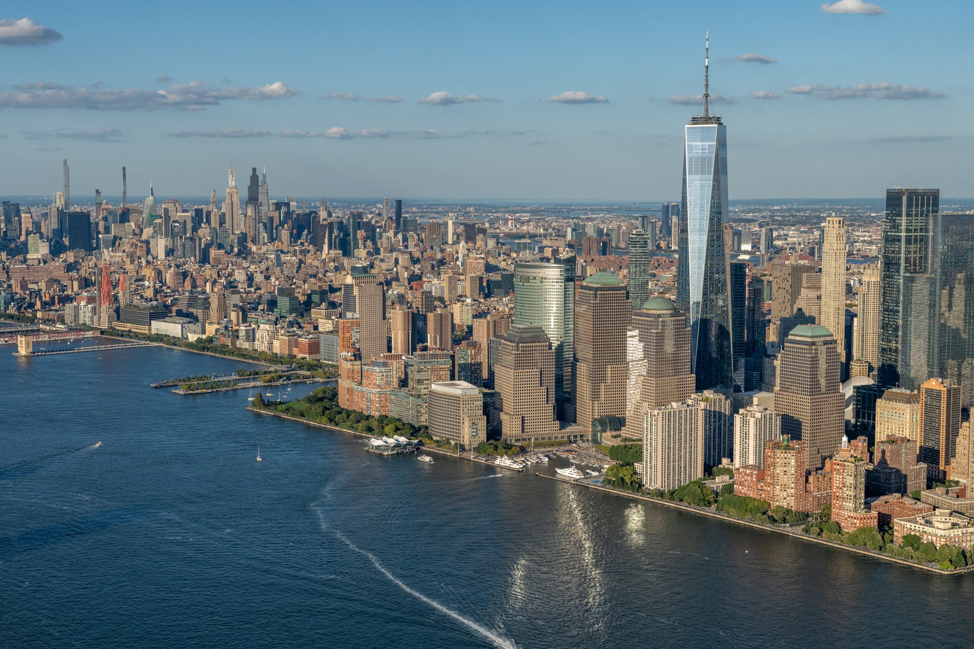 Sweeping aerial view of the downtown Manhattan skyline, featuring One World Trade Center and the Hudson River on a clear day.
